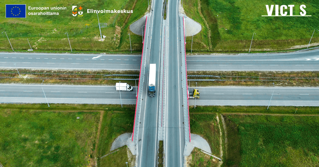 Ilmakuva maantiesillasta, joka ylittää monikaistaisen valtatien vihreän maaseutumaiseman keskellä. Tiellä kulkee kuorma-autoja. Kuvan yläreunassa ovat Euroopan unionin osarahoituksen, Elinvoimakeskuksen ja VICTIS-hankkeen logot